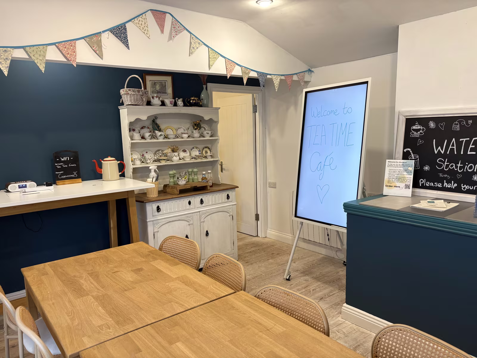 The upstairs room at Tea Time, teal wall and white dresser of teacups behind the long table, bunting across the ceiling